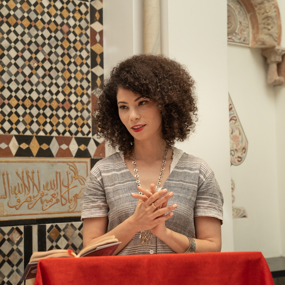 Ikram Lakhdhar headshot standing at podium with hands clasped